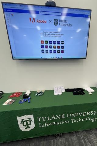 Tulane University tech display with Adobe presentation on screen and various items on a green table.